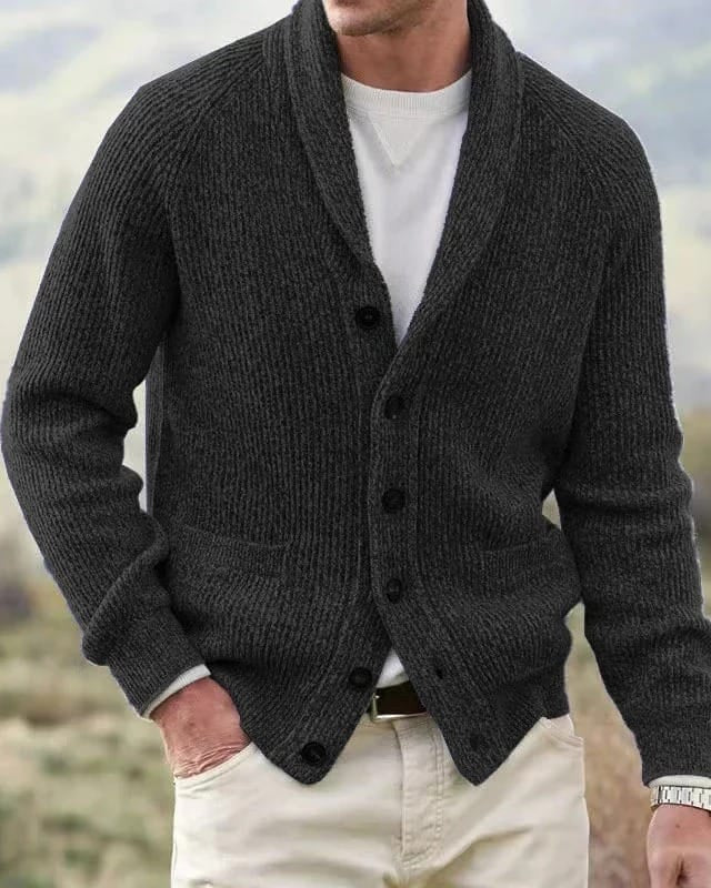Zijaanzicht van een man die het zwarte cardigan draagt, waarbij de raglanmouwen en de vloeiende drapering van het kledingstuk zichtbaar zijn.