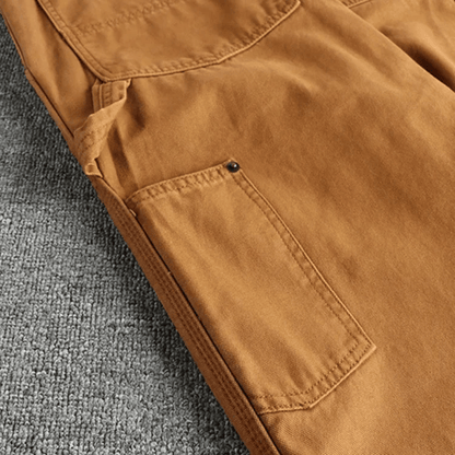 De utility broek plat gelegd, met aandacht voor de tailleband, knoopsluiting en de algehele vorm.
