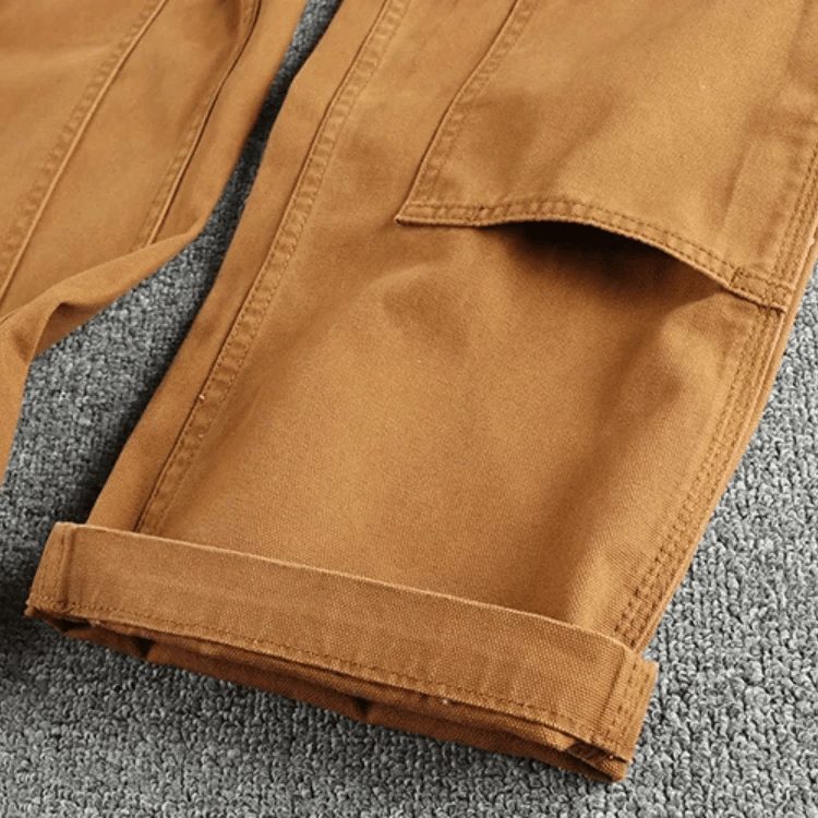 Een man in de kaki utility broek loopt langs een stadsmuur, wat de robuuste maar stijlvolle uitstraling accentueert.