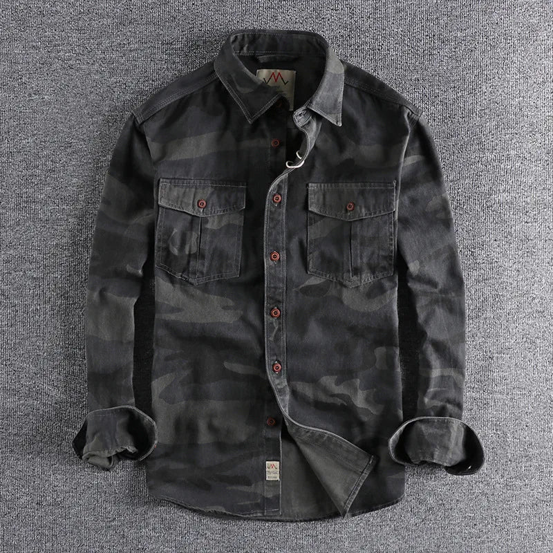 Mannelijk model draagt een camouflage T-shirt in olijfgroen, staand in een stedelijke omgeving met een ontspannen houding.