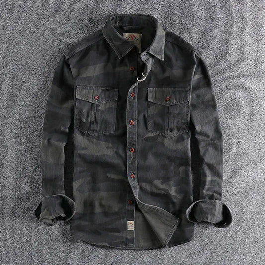 Mannelijk model draagt een camouflage T-shirt in olijfgroen, staand in een stedelijke omgeving met een ontspannen houding.