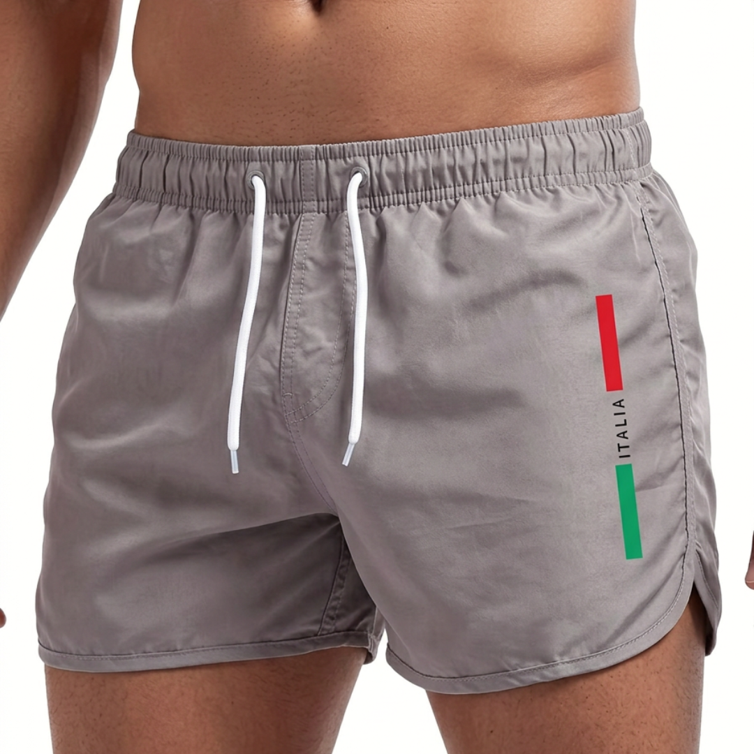 Close-up van de driekleurige 'Italia' print op de zijkant van de rode Italiaanse zwemshort, wat de Italiaanse identiteit benadrukt.